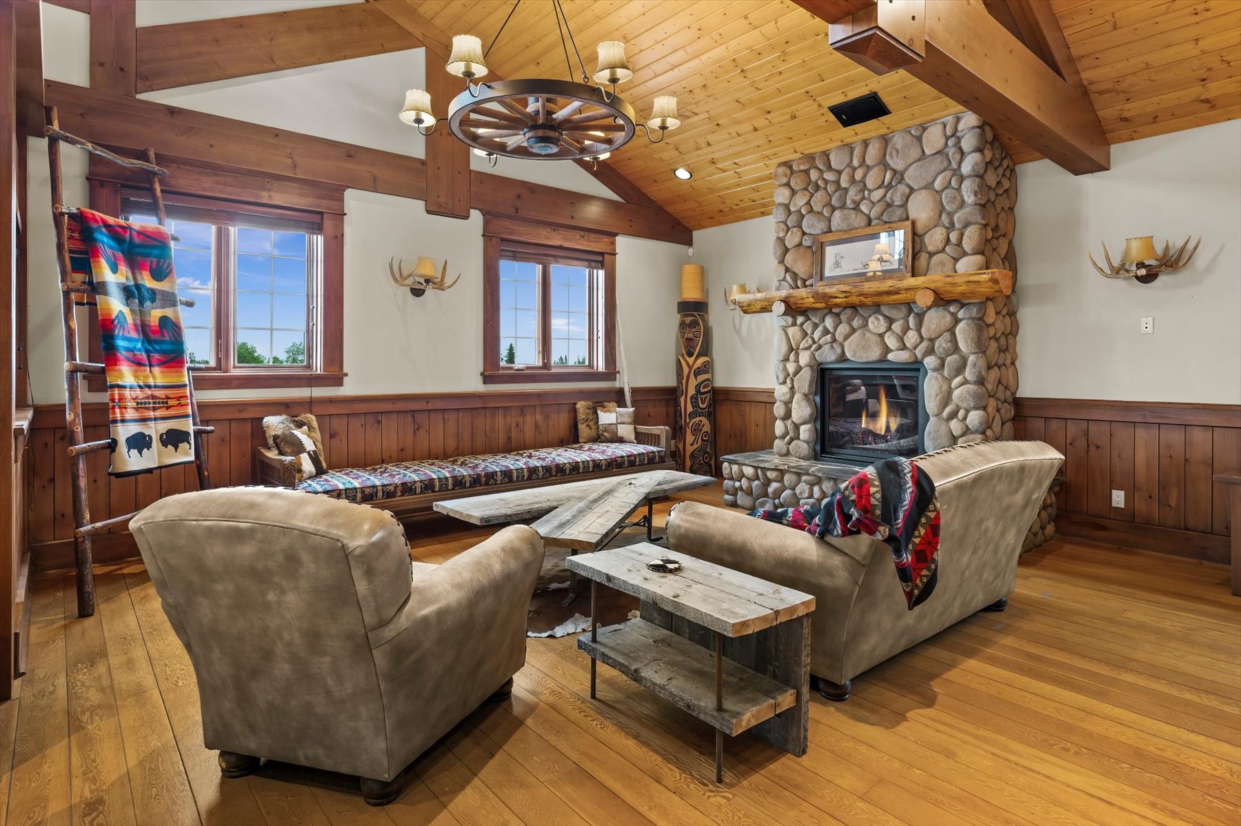 Leather club chairs facing a river-rock gas fireplace with wagon-wheel chandelier