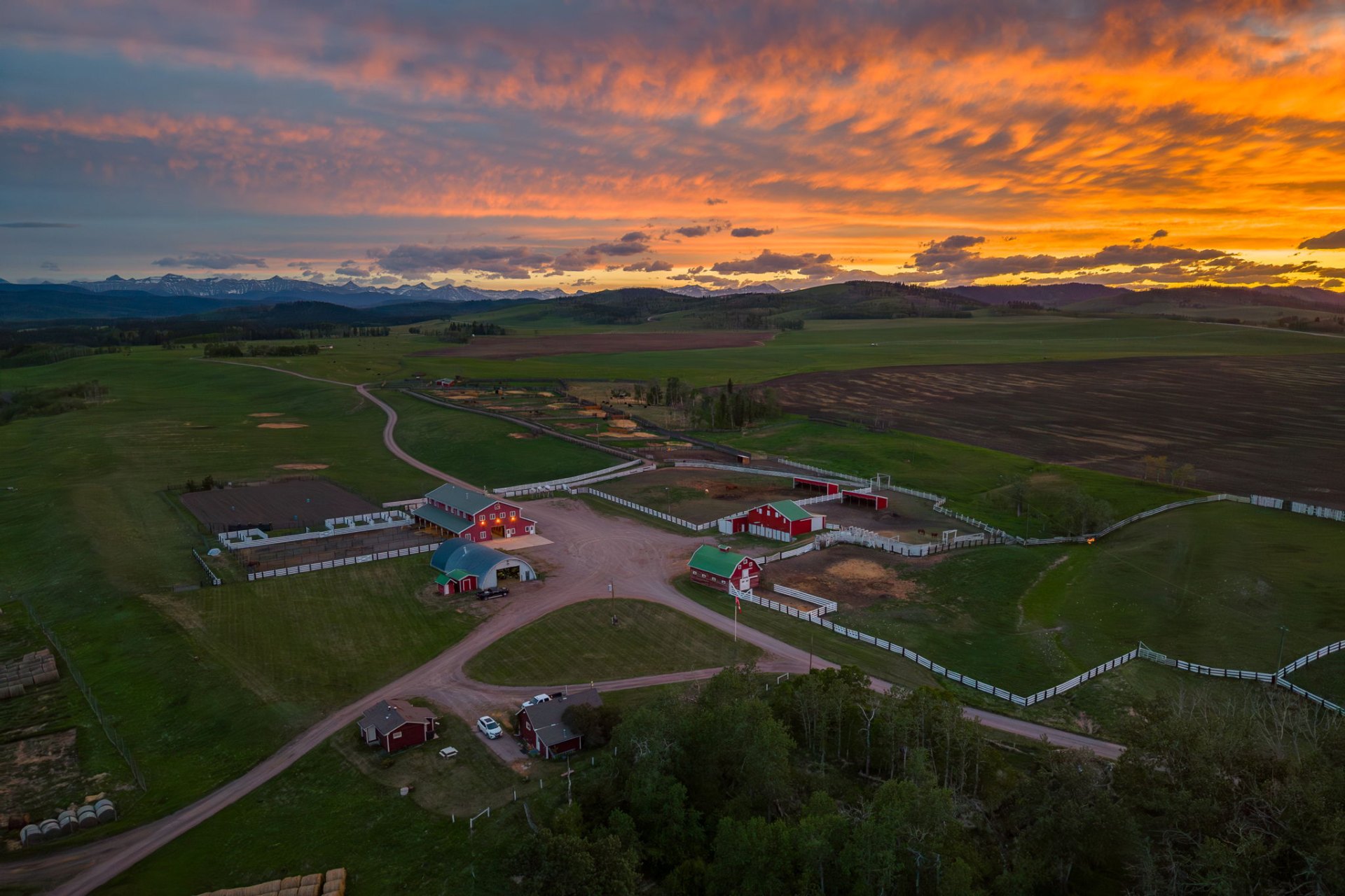 Aerial of the ranch complex at fiery sunset with the Rocky Mountains on the horizon