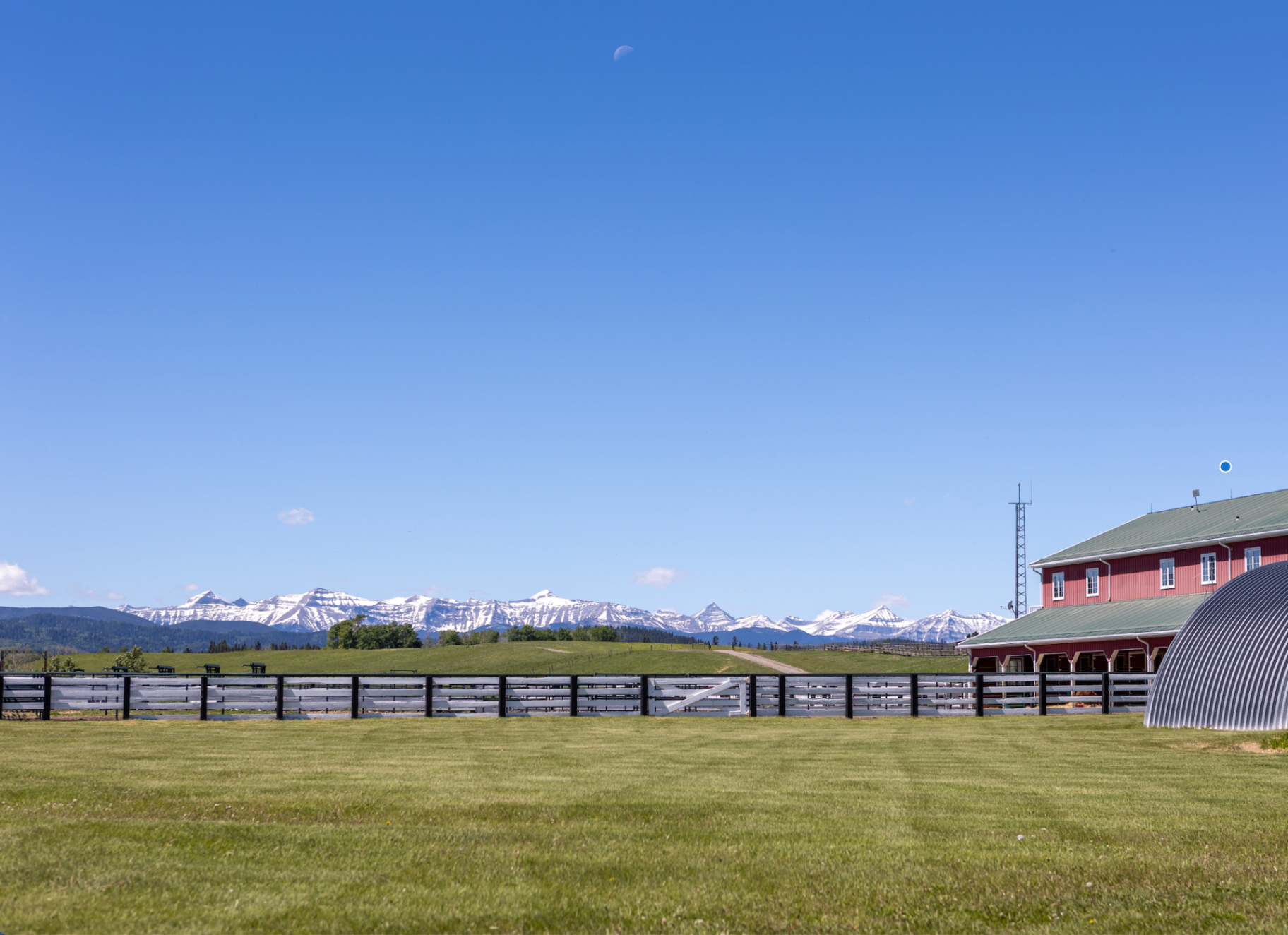 Incredible Rocky Mountain range view across the ranch with red barn and white fence line